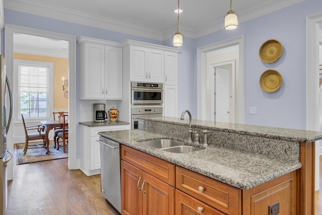 kitchen featuring a sink, appliances with stainless steel finishes, light wood-style floors, a center island with sink, and light stone counters