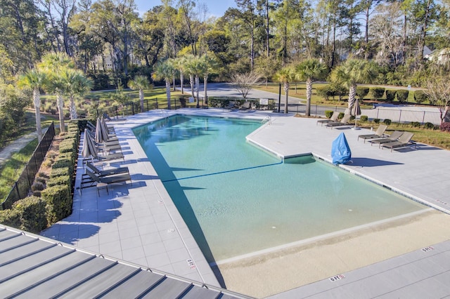 community pool featuring a patio area, fence, and view of wooded area