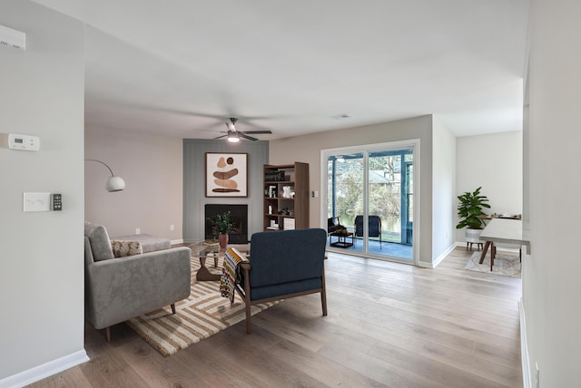 living room with light wood-type flooring, ceiling fan, and a large fireplace