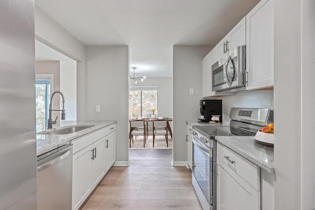 kitchen with white cabinets, stainless steel appliances, sink, backsplash, and light stone counters