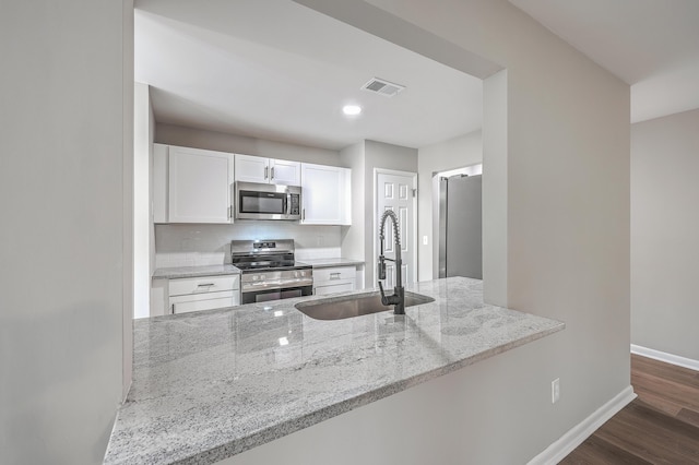 kitchen with kitchen peninsula, sink, white cabinetry, light stone countertops, and stainless steel appliances