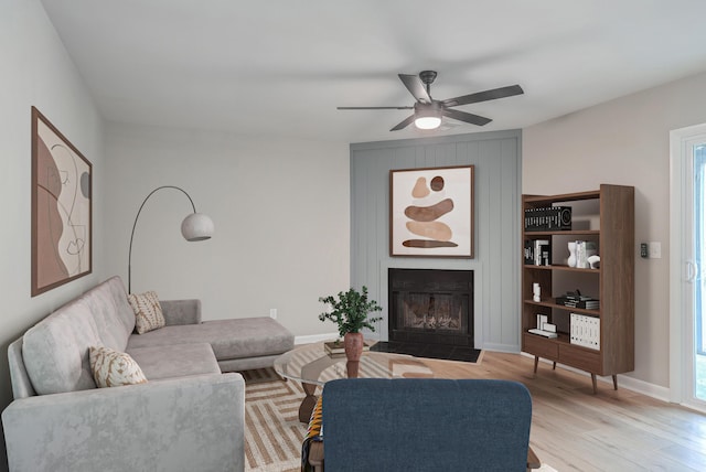 living room featuring ceiling fan, light wood-type flooring, and a fireplace