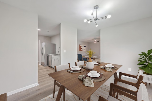 dining space featuring ceiling fan with notable chandelier, sink, and light hardwood / wood-style flooring