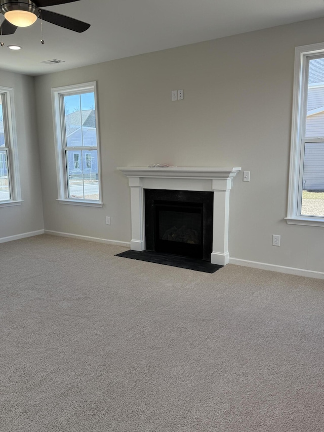 unfurnished living room with visible vents, a fireplace with flush hearth, carpet flooring, baseboards, and ceiling fan