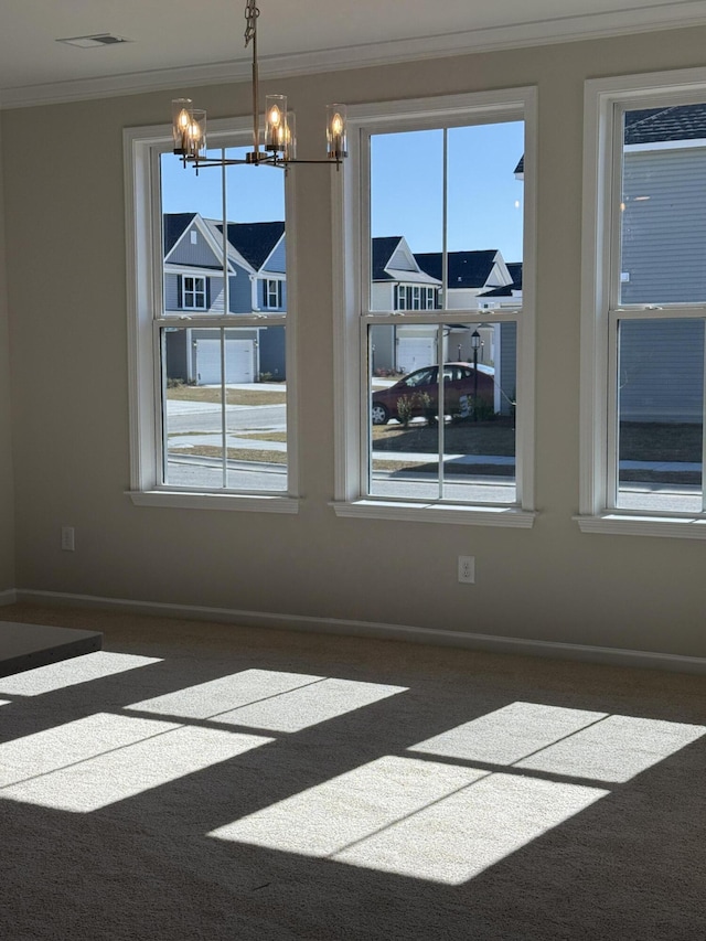 carpeted spare room with a chandelier, visible vents, baseboards, and ornamental molding