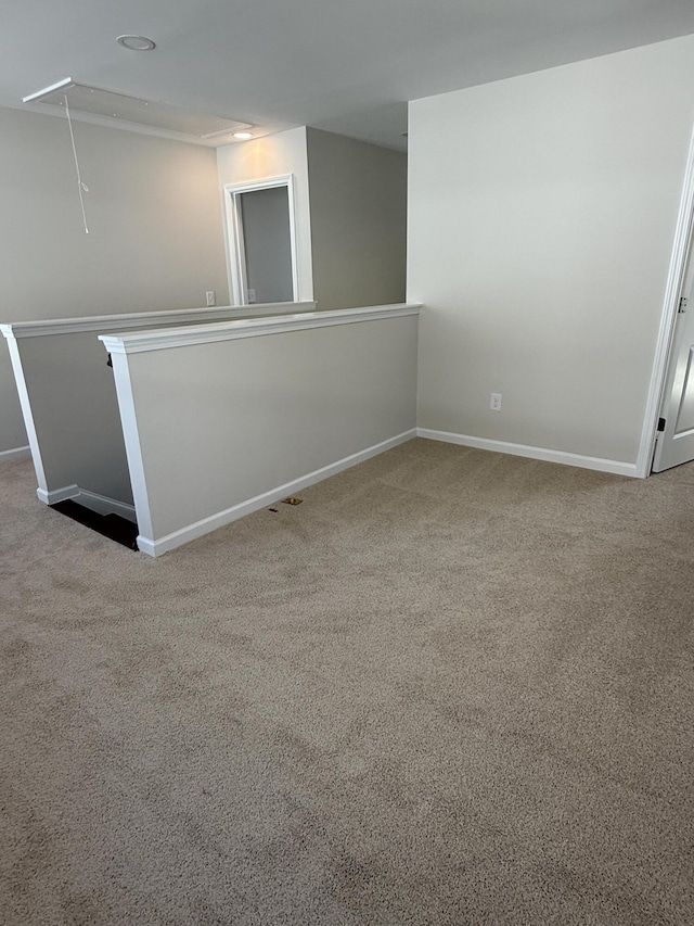 carpeted spare room featuring attic access and baseboards