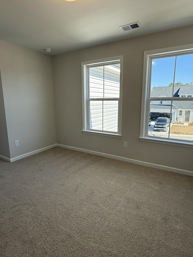 carpeted spare room featuring plenty of natural light, baseboards, and visible vents