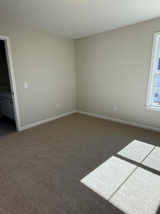 unfurnished room with baseboards and dark colored carpet