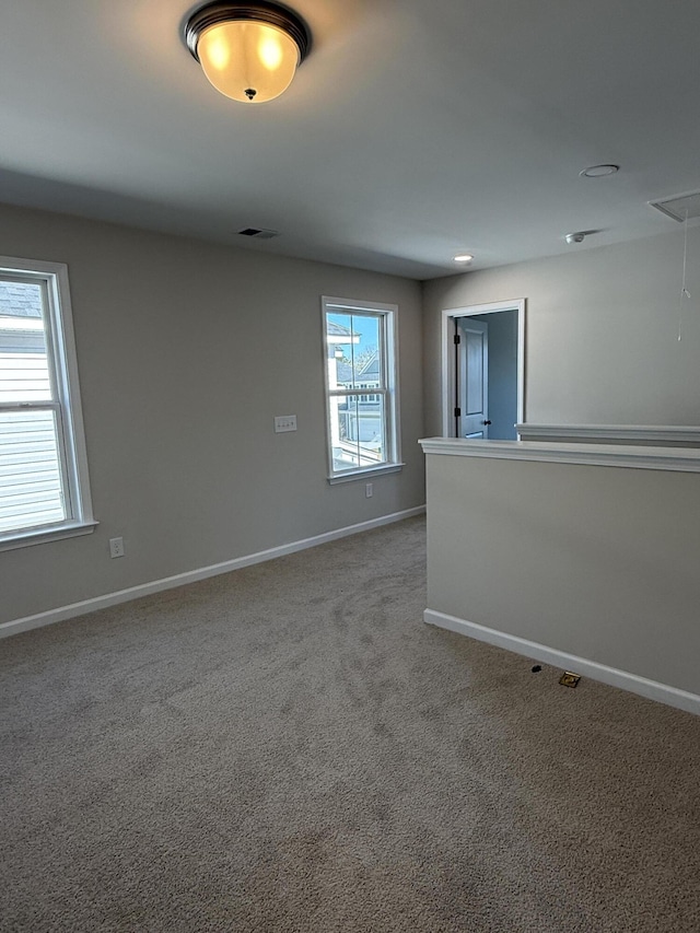 carpeted empty room with attic access, visible vents, and baseboards