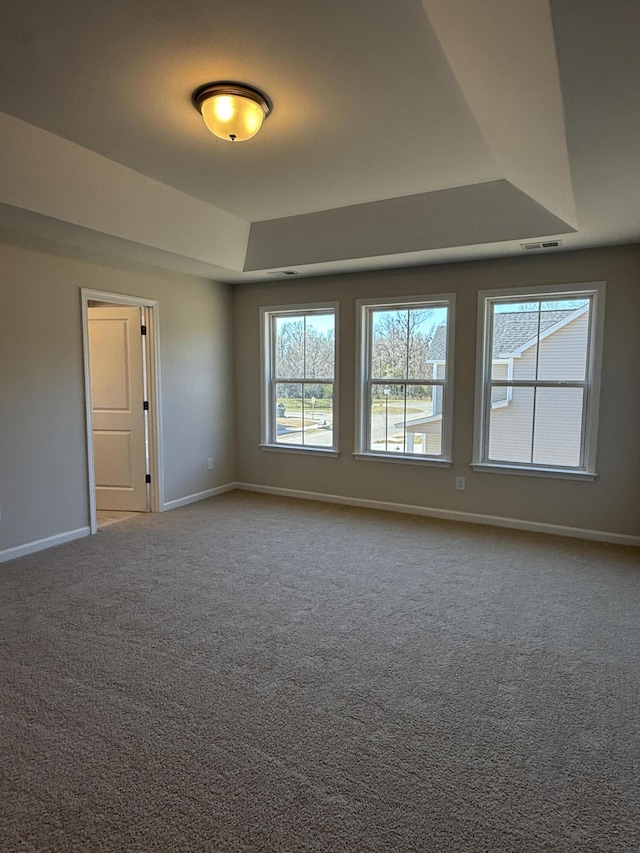 carpeted spare room with a raised ceiling, visible vents, and baseboards