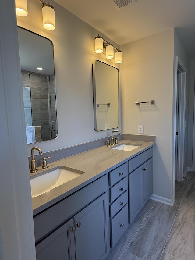 bathroom featuring double vanity, a stall shower, baseboards, and a sink