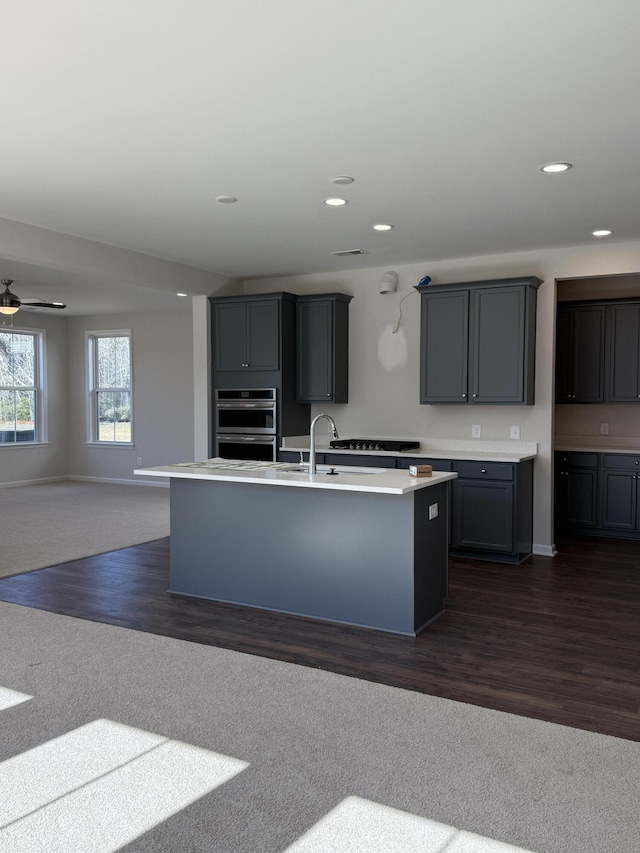 kitchen with stainless steel double oven, dark wood finished floors, a sink, light countertops, and open floor plan