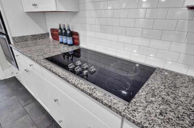 kitchen featuring white cabinetry, light stone countertops, tasteful backsplash, dark tile patterned flooring, and black electric stovetop