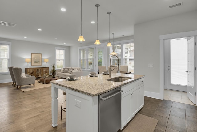 kitchen featuring white cabinets, stainless steel dishwasher, pendant lighting, sink, and a kitchen island with sink