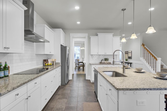 kitchen with a center island with sink, white cabinets, pendant lighting, and wall chimney range hood