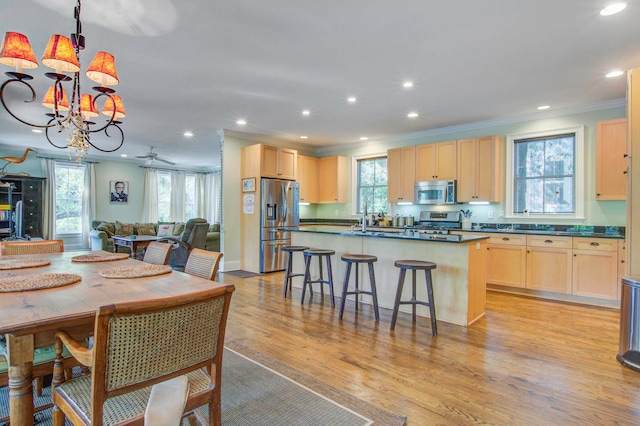 kitchen with pendant lighting, light wood-type flooring, light brown cabinets, ornamental molding, and appliances with stainless steel finishes