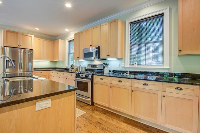 kitchen featuring light wood-type flooring, light brown cabinetry, ornamental molding, stainless steel appliances, and dark stone countertops