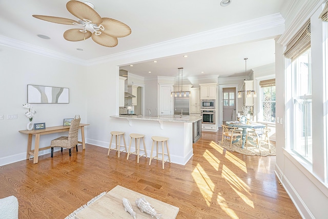 kitchen with a kitchen bar, light wood-style flooring, light stone counters, a peninsula, and built in appliances