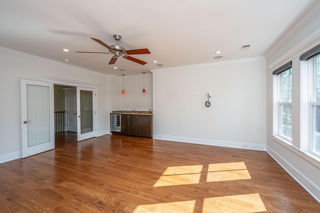 interior space featuring wood finished floors, visible vents, baseboards, ceiling fan, and crown molding