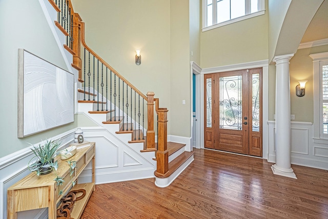 foyer featuring a decorative wall, wood finished floors, stairs, and decorative columns