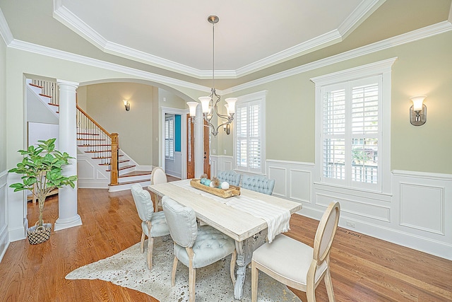 dining space featuring stairs, an inviting chandelier, wood finished floors, arched walkways, and ornate columns