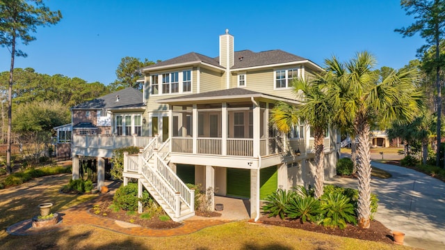 rear view of property featuring stairs, a sunroom, driveway, and a shingled roof