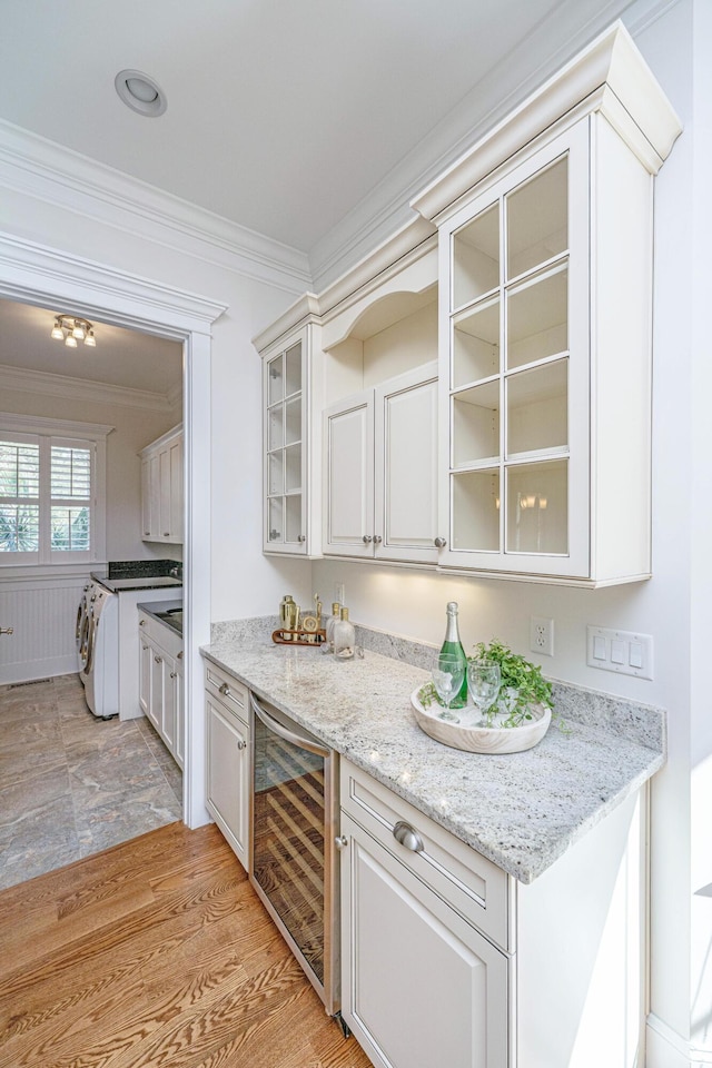 kitchen featuring ornamental molding, washing machine and dryer, wine cooler, light wood-style floors, and glass insert cabinets