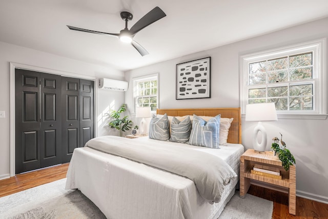 bedroom with a closet, a wall unit AC, hardwood / wood-style flooring, and ceiling fan