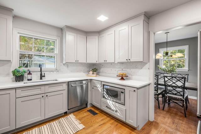 kitchen with light hardwood / wood-style floors, stainless steel appliances, sink, and decorative light fixtures