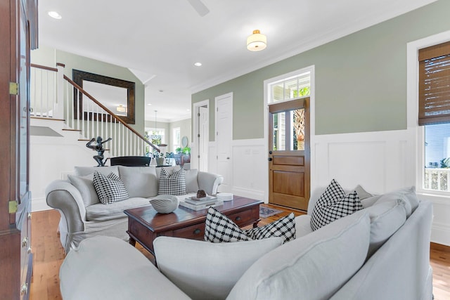 living room featuring an inviting chandelier, crown molding, a healthy amount of sunlight, and light hardwood / wood-style flooring