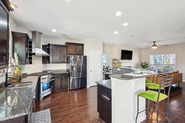 kitchen with appliances with stainless steel finishes, stone countertops, wall chimney range hood, and a center island