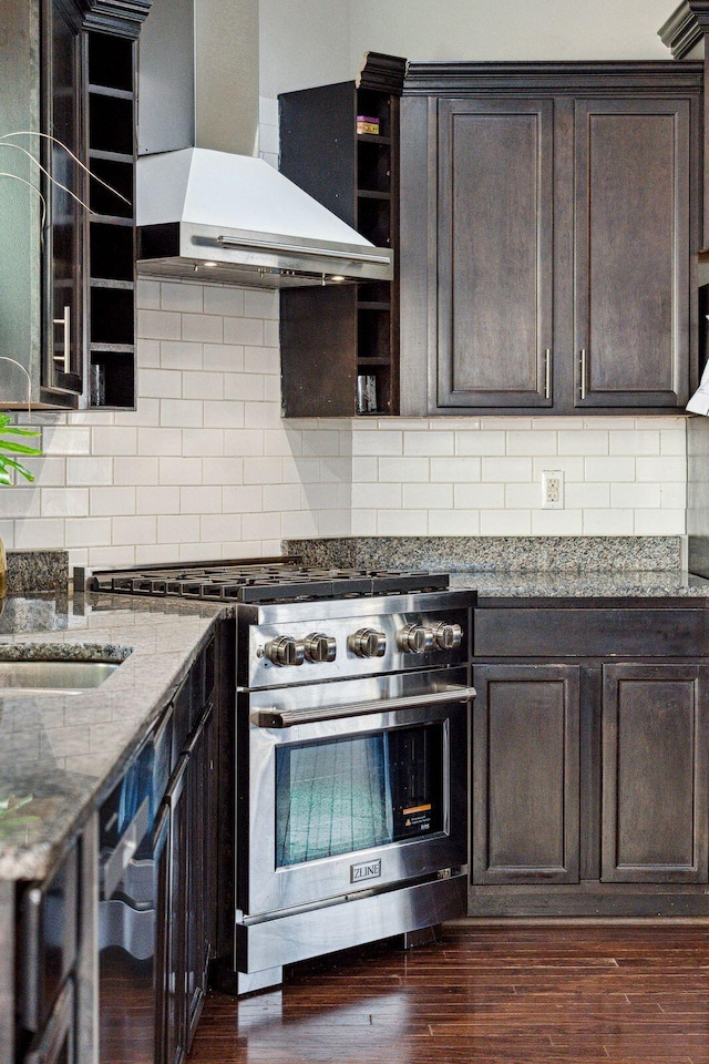 kitchen featuring light stone counters, stainless steel stove, wall chimney range hood, tasteful backsplash, and dark brown cabinets