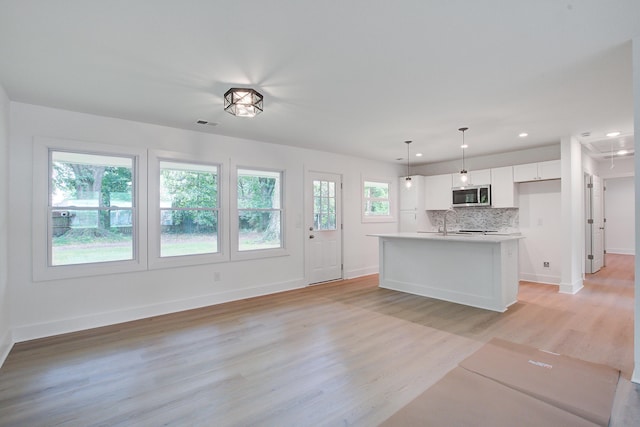 2135 Clayton St, Charleston, SC 29414 - kitchen featuring stainless steel microwave, light wood-style floors, white cabinetry, backsplash, and a sink