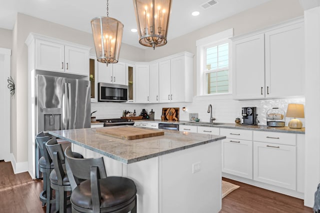 kitchen with appliances with stainless steel finishes, sink, a kitchen island, pendant lighting, and white cabinets