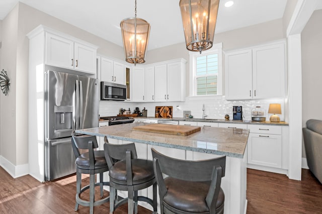 kitchen with appliances with stainless steel finishes, a kitchen island, white cabinetry, decorative light fixtures, and dark hardwood / wood-style floors