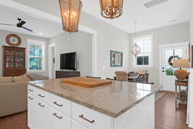 kitchen featuring dark hardwood / wood-style floors, a center island, pendant lighting, white cabinetry, and light stone counters