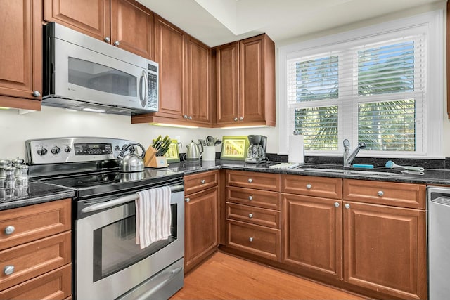 kitchen with appliances with stainless steel finishes, sink, light hardwood / wood-style flooring, and dark stone countertops