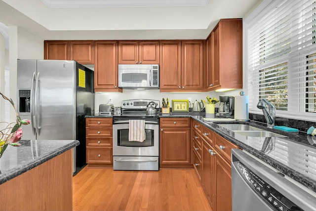 kitchen with dark stone countertops, sink, light wood-type flooring, and appliances with stainless steel finishes