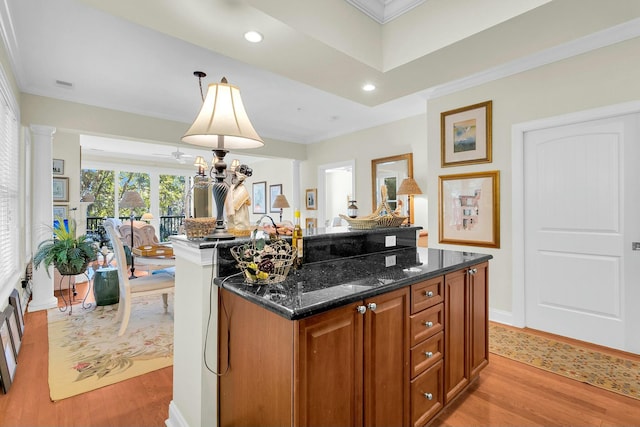 kitchen featuring hanging light fixtures, light wood-type flooring, dark stone countertops, ornamental molding, and a kitchen island