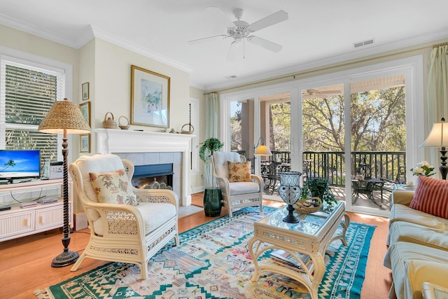 living room featuring a tiled fireplace, crown molding, wood-type flooring, and ceiling fan