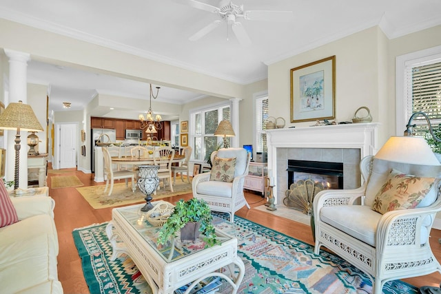 living room featuring ornate columns, ceiling fan with notable chandelier, a fireplace, light hardwood / wood-style floors, and crown molding