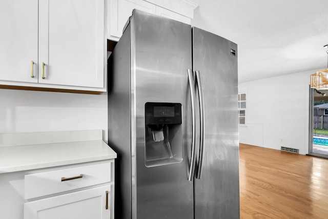 kitchen with white cabinetry, stainless steel fridge, light hardwood / wood-style floors, and hanging light fixtures