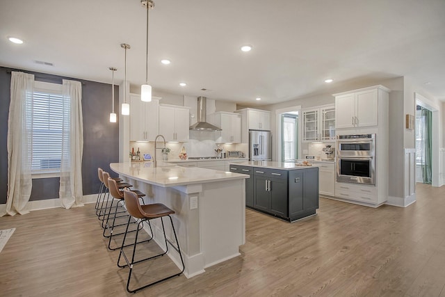 kitchen with white cabinetry, stainless steel appliances, kitchen peninsula, and wall chimney exhaust hood