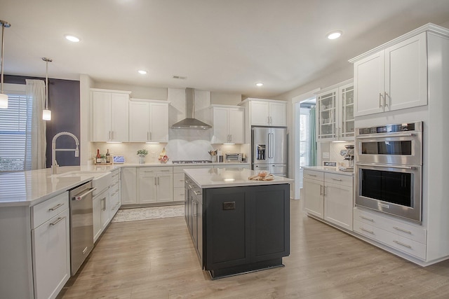 kitchen featuring appliances with stainless steel finishes, white cabinetry, hanging light fixtures, a center island, and wall chimney exhaust hood