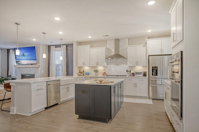 kitchen with wall chimney range hood, hanging light fixtures, stainless steel appliances, a center island, and kitchen peninsula