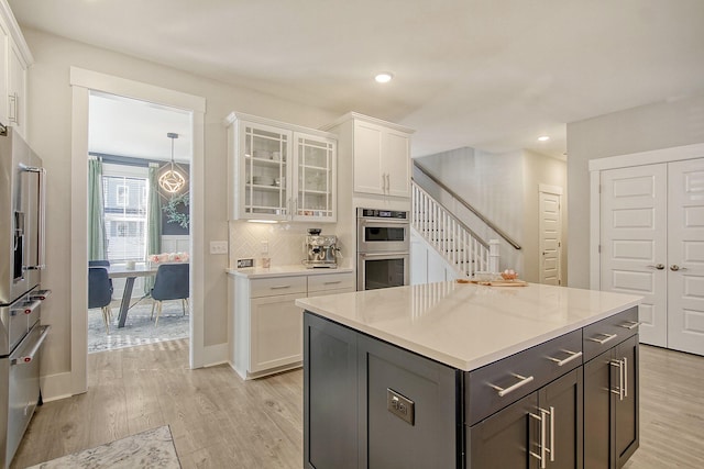 kitchen with double oven, tasteful backsplash, white cabinets, a center island, and light wood-type flooring