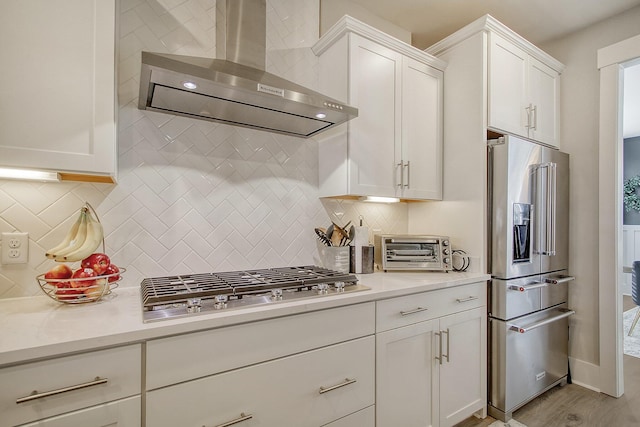 kitchen featuring wall chimney exhaust hood, stainless steel appliances, tasteful backsplash, and white cabinets