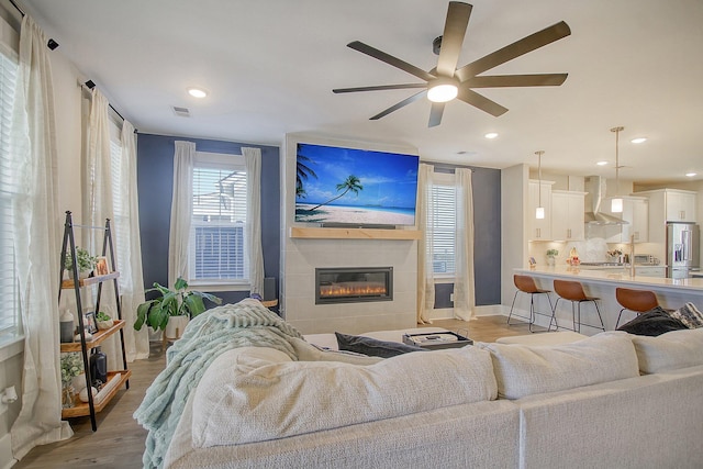 living room with a tiled fireplace, ceiling fan, and light hardwood / wood-style floors