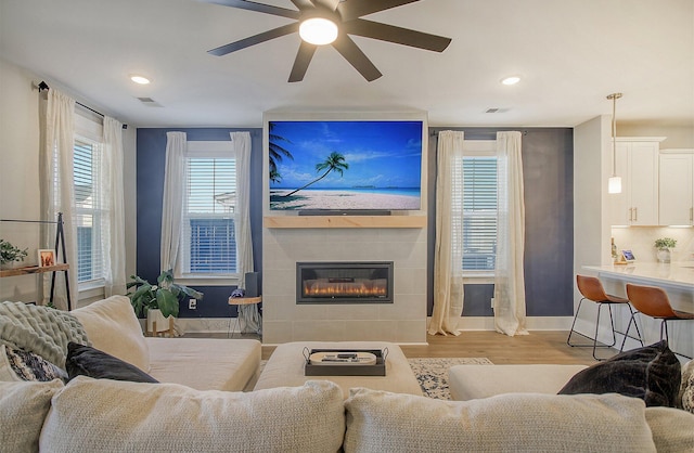 living room with ceiling fan, light hardwood / wood-style floors, a tile fireplace, and a wealth of natural light