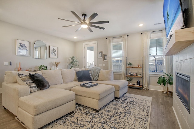 living room featuring a tiled fireplace, wood-type flooring, and ceiling fan